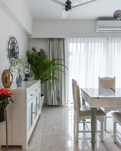 Bright dining room with marble-top table, painted chairs, white sideboard and potted palm near sheer-curtained window