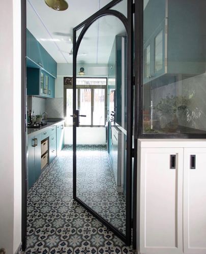 Teal galley kitchen viewed through an arched black-framed glass door with patterned cement tile floor