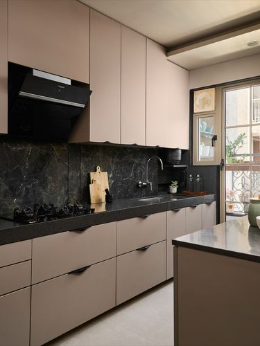 Blush pink kitchen with black stone backsplash, countertop, chimney hood, and glass balcony door