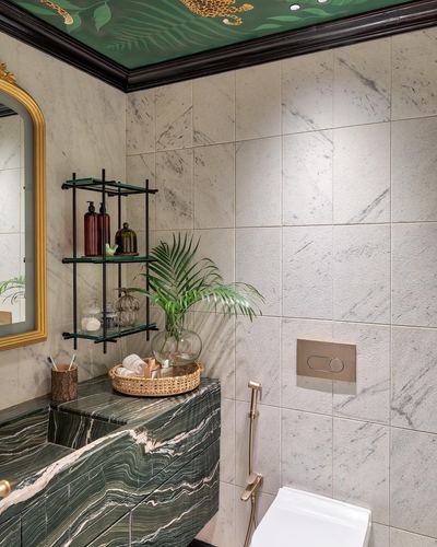 Bathroom corner with green marbled vanity, gold mirror, black shelving and painted leopard-print ceiling