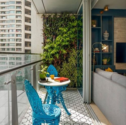 Turquoise cast-iron bistro set on patterned tile balcony with vertical garden wall, city view beyond