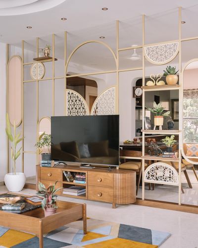 Living room with fluted wood TV unit beneath a brass and jali partition screen dividing dining area