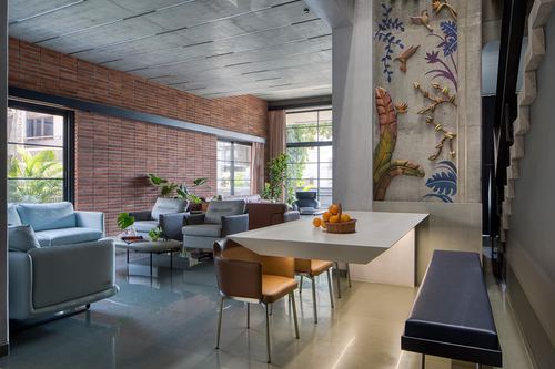 Open living-dining space with brick wall, concrete ceiling, and decorative relief mural on pillar