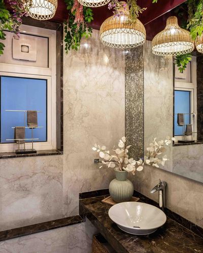 Mumbai powder room with marble walls, dark countertop vessel sink, and rattan pendant lights draped with greenery