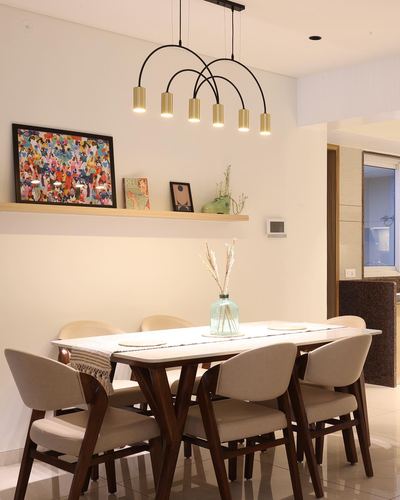 Dining table under arched brass pendant lights, floating shelf with art above