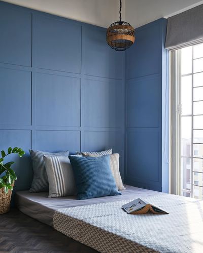 Low bed with striped and checked cushions against a blue paneled wall, cane pendant light above