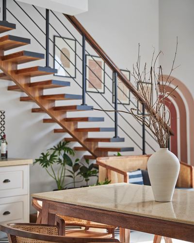 Floating wooden staircase beside terrazzo table with large ceramic vase and cane armchair.