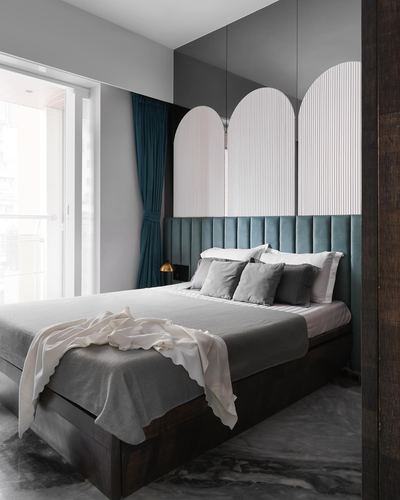 Bedroom with teal channel-tufted headboard, arched fluted panels, mirrored wall, and marble floor