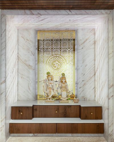 Marble pooja niche with backlit gold jali panel, deity idols, and walnut drawer cabinetry below