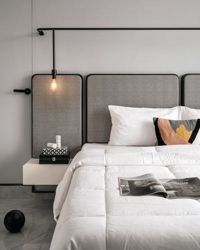 Grey upholstered headboard panels with a hanging bulb pendant beside a white-linen bed