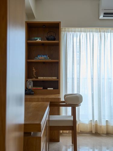 Wooden study nook with open shelving, desk, chair, and sheer curtained window