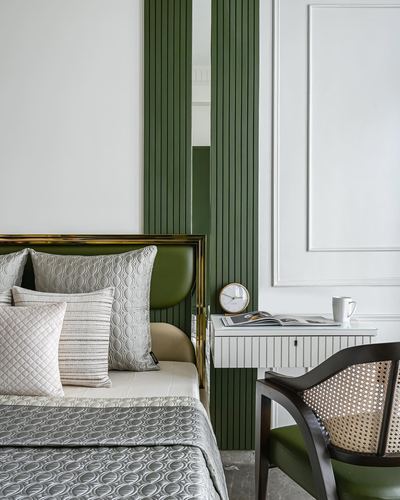 Bedroom corner with green upholstered brass-edged headboard, fluted green panels, and cane armchair by floating nightstand