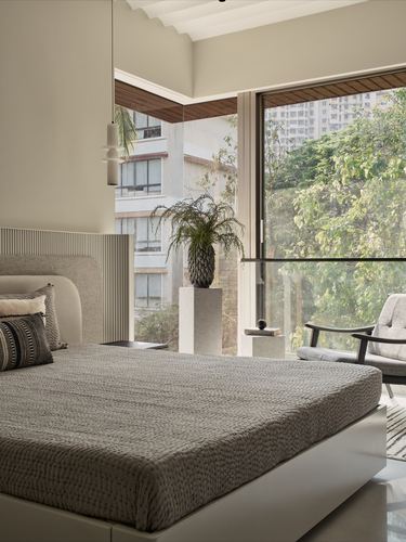 Minimalist bedroom with grey bed, ribbed headboard, and floor-to-ceiling window overlooking trees and buildings