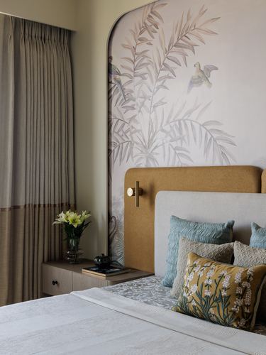 Bedroom with mustard and grey upholstered headboard beneath an arched bird-and-leaf mural panel