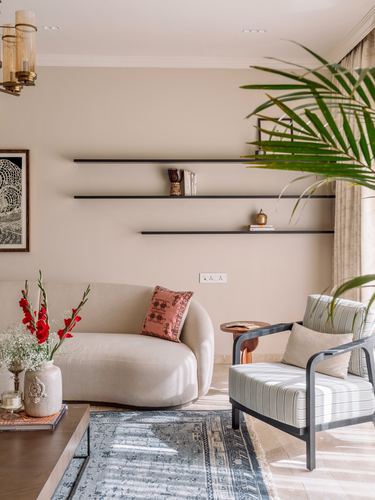 Beige living room with curved sofa, cane armchair, floating shelves and patterned rug
