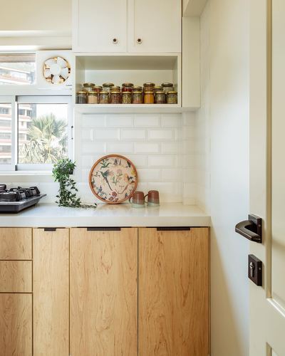 Corner of a white and wood kitchen with spice jars, tiled backsplash, and a decorative plate