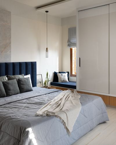 Bedroom with navy channel headboard, grey linens, window seat and glossy wardrobe under soft daylight