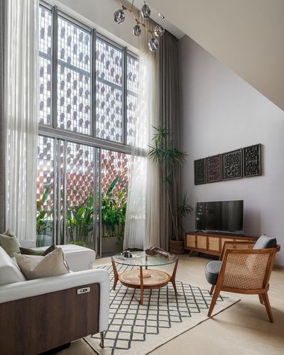 Double-height living room with jali window, cane armchair and wooden TV console