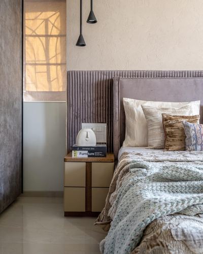 Bedroom corner with fluted mauve headboard, pendant lights, and layered pillows beside a wooden nightstand