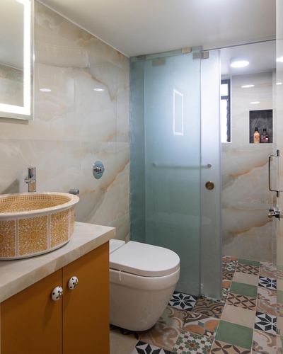 Bathroom with veined stone walls, mustard vanity, patterned tile floor and frosted glass shower