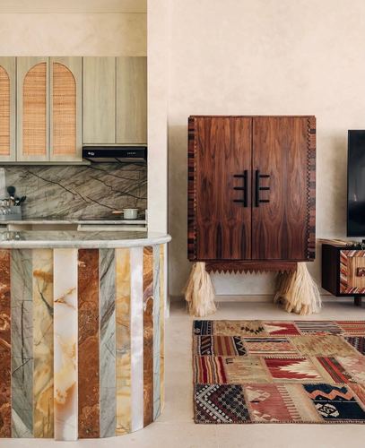 Curved striped-stone kitchen island beside a dark wood cabinet with fringed legs and a patchwork rug