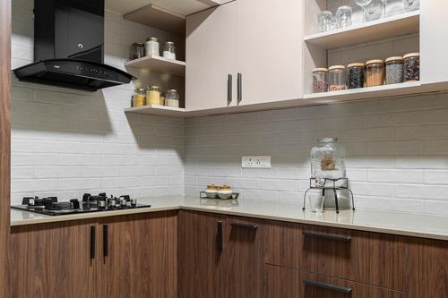 Modern kitchen corner with wood cabinets, white tiled backsplash, black chimney and open shelves with jars