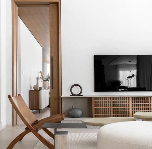 Minimalist living room with woven wood tv console, leather folding chair, and open sliding door to hallway