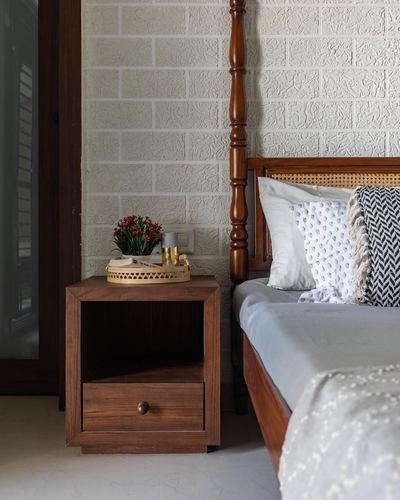 Wooden four-poster bed with cane headboard beside a dark wood nightstand against a textured wall