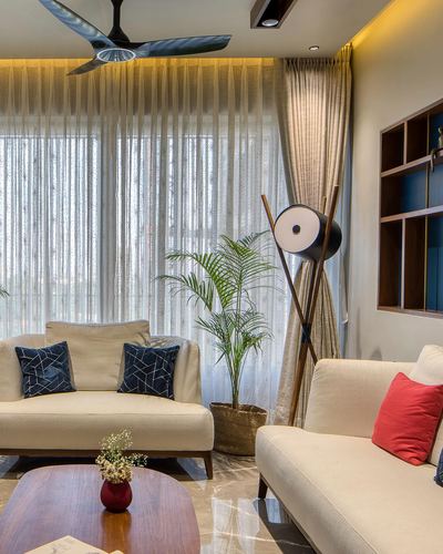 Living room with cream sofas, blue cushions, sheer curtains, and a tripod floor lamp near a window