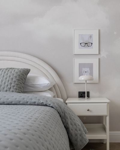 Toddler bedroom with curved upholstered headboard, grey bedding, and framed animal prints above a white nightstand