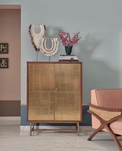 Brass-studded cabinet with decorative objects on top against a color-blocked blue and peach wall