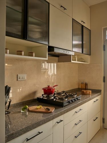 Cream galley kitchen with reeded glass cabinets, granite counter, red pot on gas stove