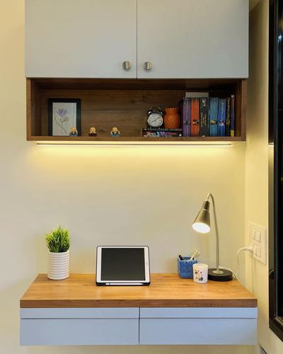 Floating wooden desk under wall-mounted cabinets with lit open shelf holding books and decor