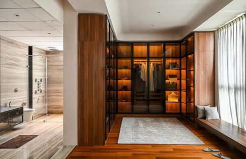 Walk-in wardrobe with black-framed glass doors flanked by wood paneling, opening to marble bathroom beyond