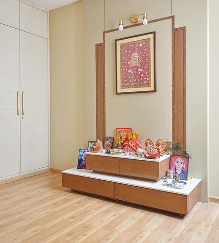Pooja unit with idols and framed miniature art set into a wood-framed wall niche