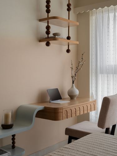 Floating wood desk with fluted front beneath ball-strung wall shelves in a beige bedroom