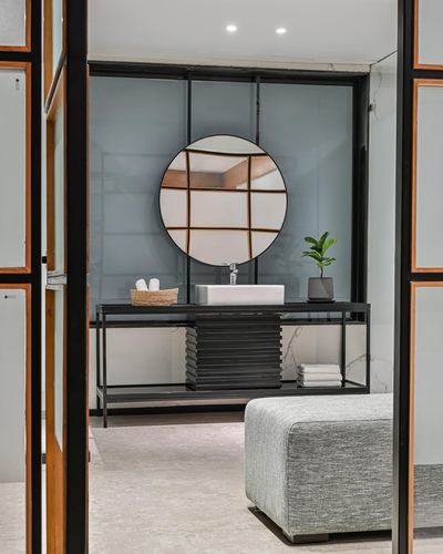 View through glass doors into a bathroom with round mirror and black vanity console
