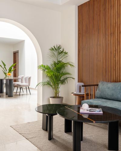 Living room with fluted wood wall, teal sofa, black round tables, arch to dining beyond