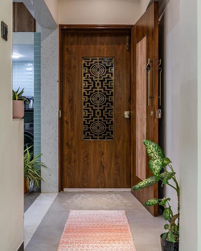 Wooden entrance door with brass lattice inset, concrete floor, foyer with plants and pink runner