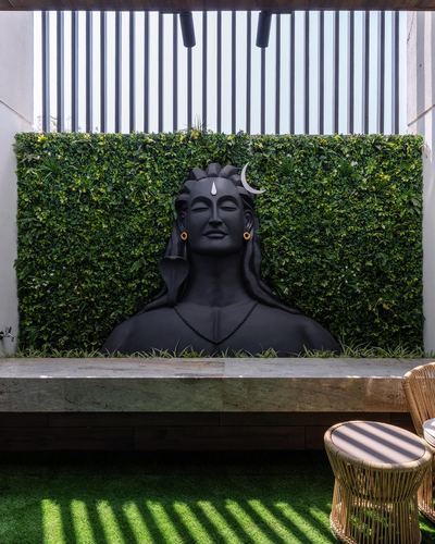 Black Shiva bust sculpture against a green wall in a terrace with stone bench and cane stools