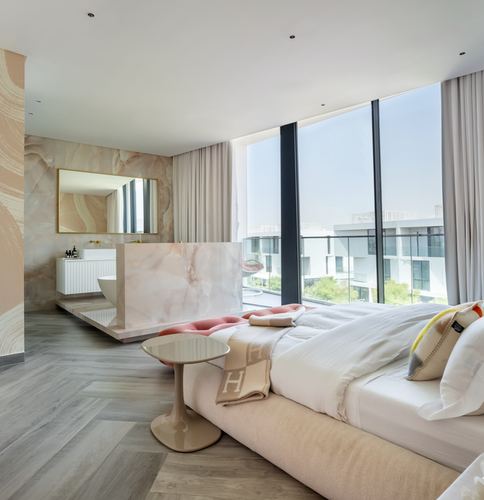 Open-plan bedroom with veined stone bathtub wall, herringbone floor, and floor-to-ceiling windows