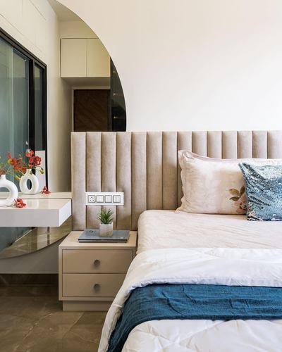 Beige channel-tufted headboard bed with teal cushion beside arched mirrored niche and marble floor