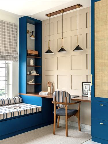 Blue built-in study nook with window seat, paneled wall, and three pendant lights over a desk