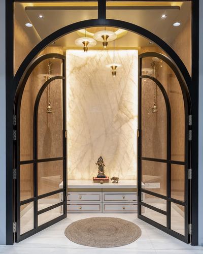 Arched black glass doors open into a backlit pooja niche with stone panel and idol