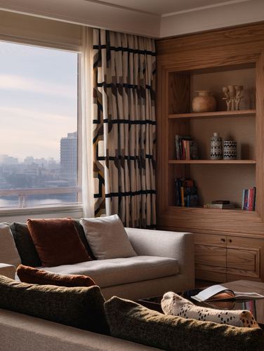 Living room corner with wood shelving, patterned curtain, and river view through window
