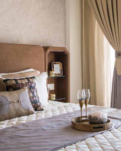 Bed with woven leather cushions, champagne flutes on a wooden tray, curved wooden nightstand with glass shelves