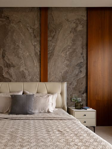 Bedroom headboard against a veined stone wall with wood inlay strips and a bedside table
