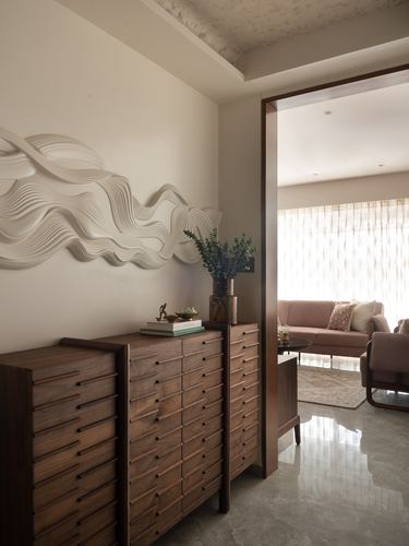 Foyer with wavy textured wall art above a wooden multi-drawer dresser, opening to a pink sofa living room