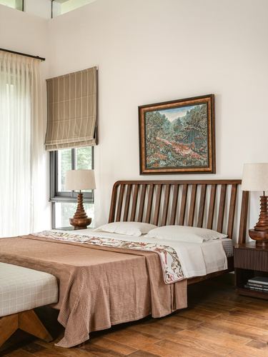 Bedroom with slatted wood headboard, framed landscape painting, and turned wood lamps on either side