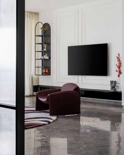 Living room with maroon leather armchair, wall-mounted TV, and arched black shelving unit on polished marble floor